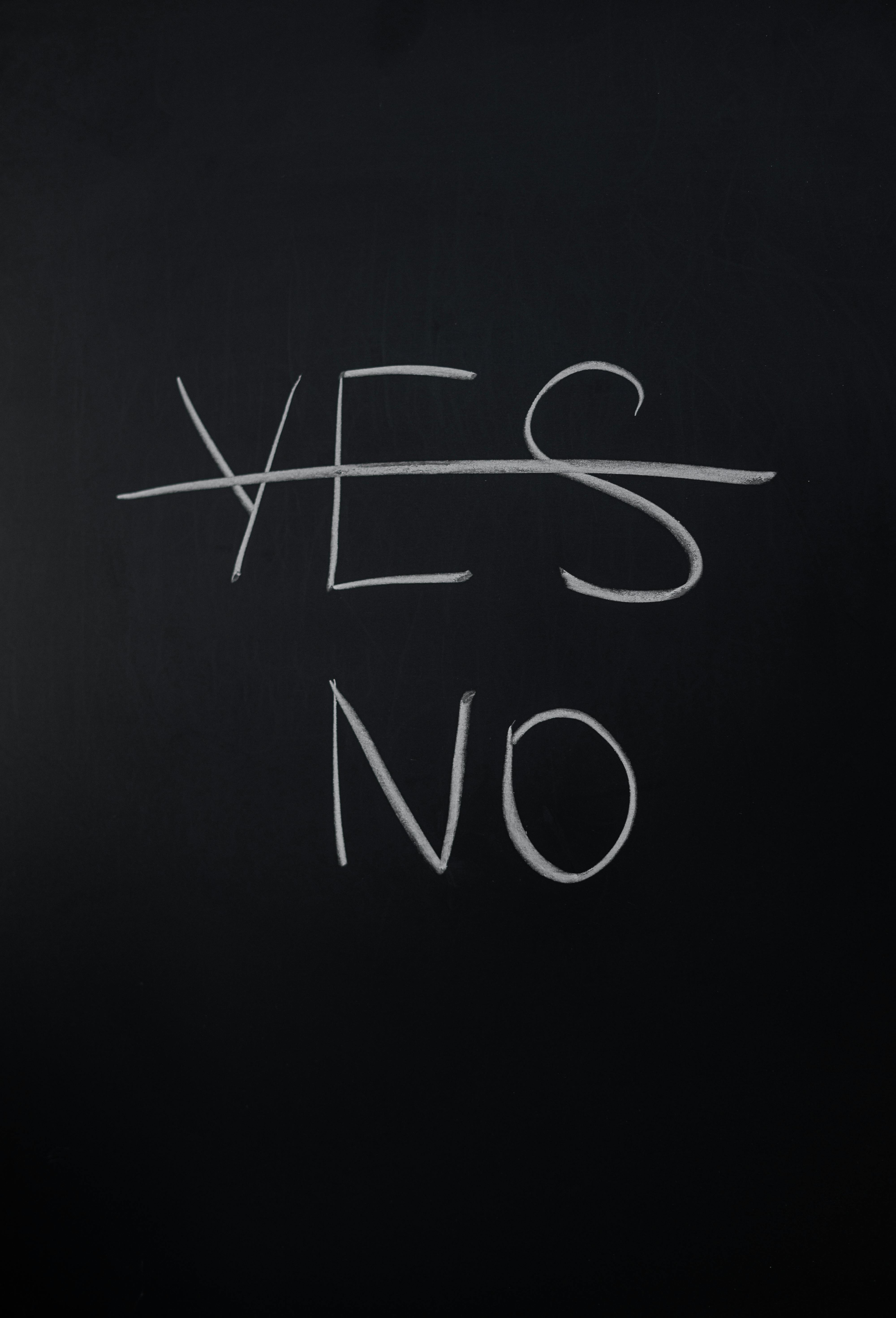 The word 'YES' crossed out and 'NO' written beneath it on a blackboard — a bold visual statement of refusal, decision-making, or setting boundaries.
